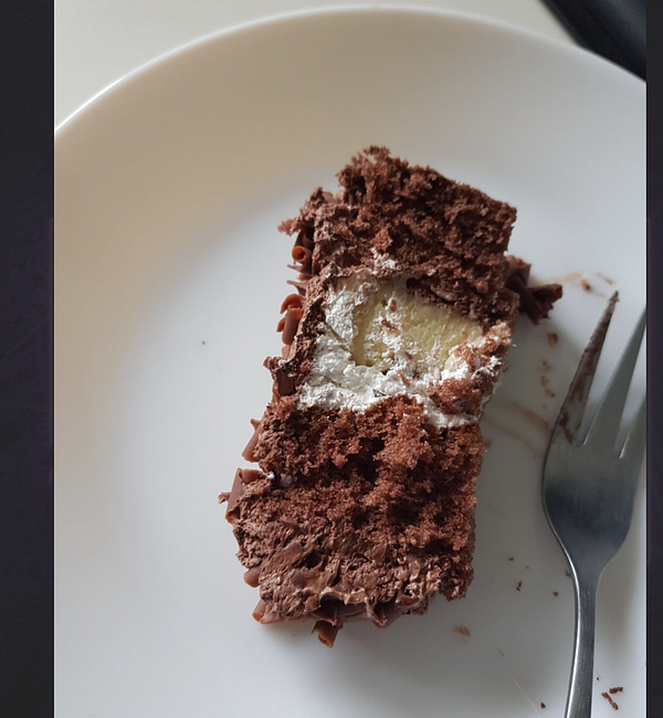 A slice of chocolate birthday cake is displayed on a white plate with a fork beside it.