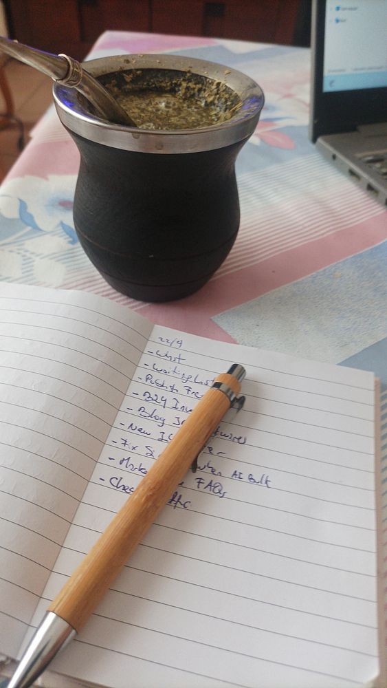 A cozy workspace featuring a traditional mate cup, a notebook with a to-do list, and a laptop.