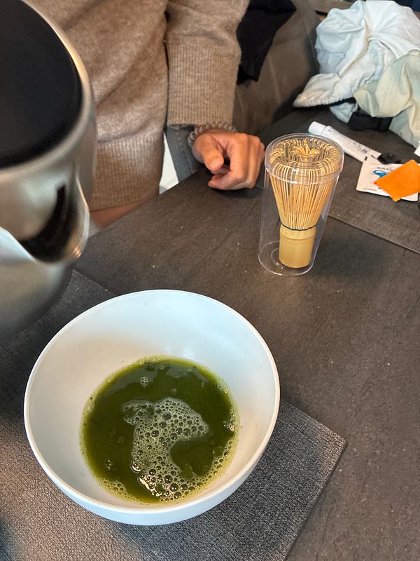 Preparation of homemade matcha latte with a bowl of matcha tea, bamboo whisk, and kettle for hot water.