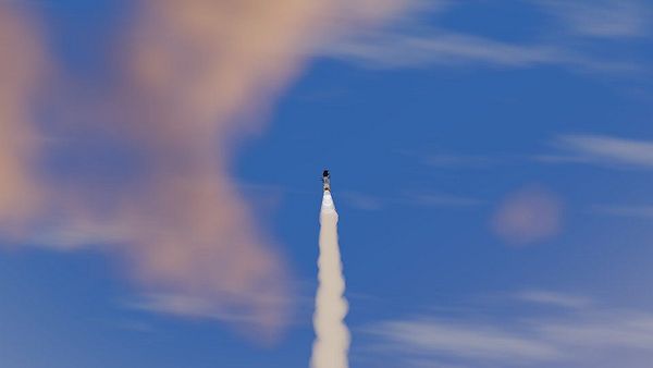A rocket ascending with a trail of exhaust against a partly cloudy sky.