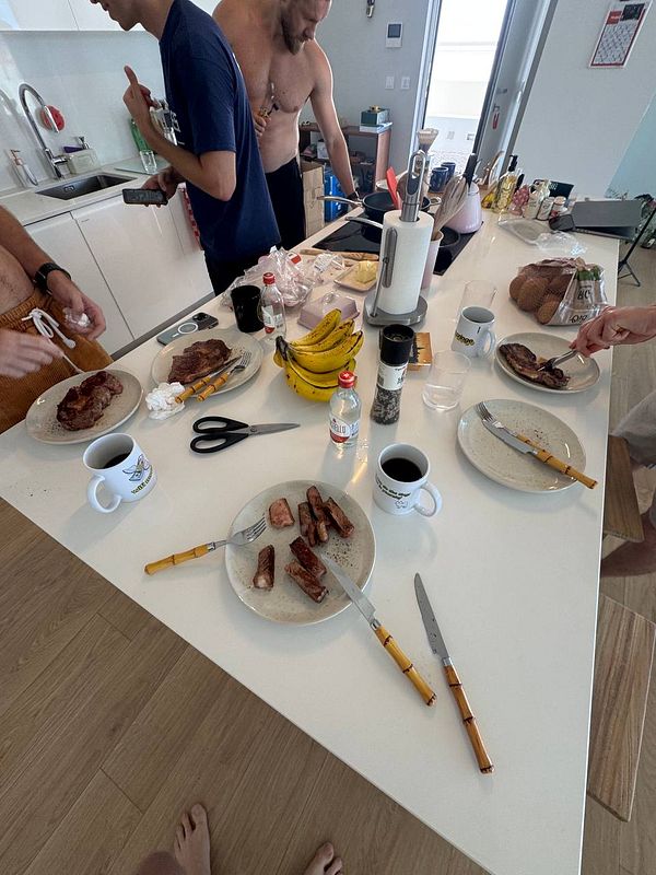 A group of people is preparing and enjoying a meal of steak in a modern kitchen.