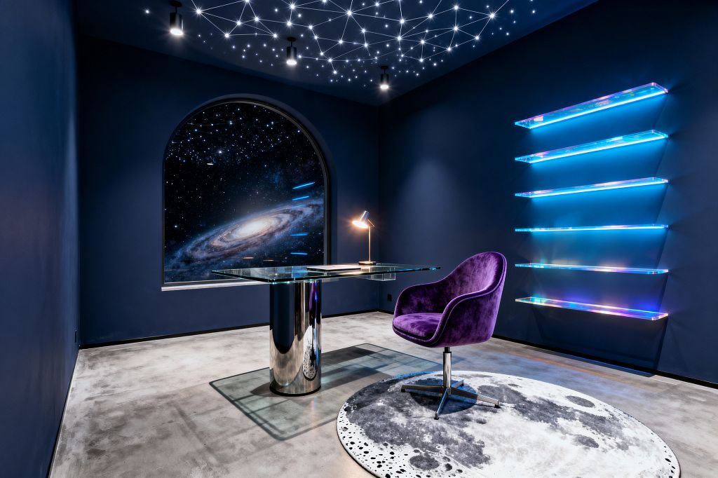 A home office with deep navy walls features a starry ceiling made of fiber‑optic constellation lights and small black downlights. An arched opening shows a large galaxy graphic. A clear glass desk with a mirrored chrome cylindrical base holds a brass desk lamp. A purple velvet swivel chair sits on a round moon‑printed rug over polished concrete flooring. On the right wall, five floating iridescent acrylic shelves glow in blue and magenta tones.