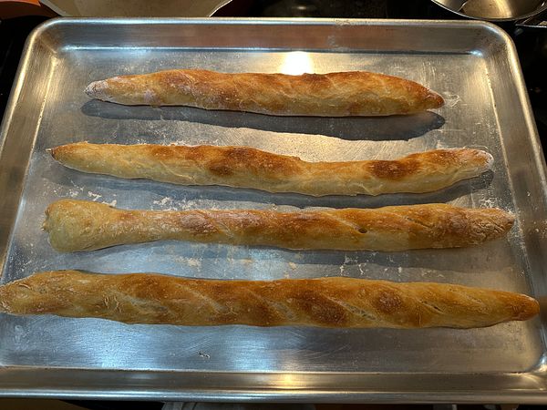 Four freshly baked baguettes are arranged on a baking tray.