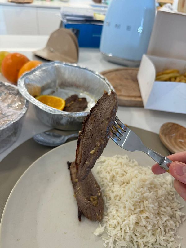 A plate of well-done picanha meat served with rice and garnished with an orange slice.