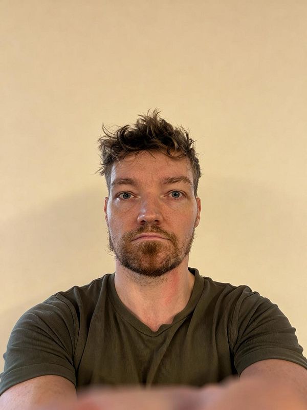 A man is taking a selfie against a plain beige background.