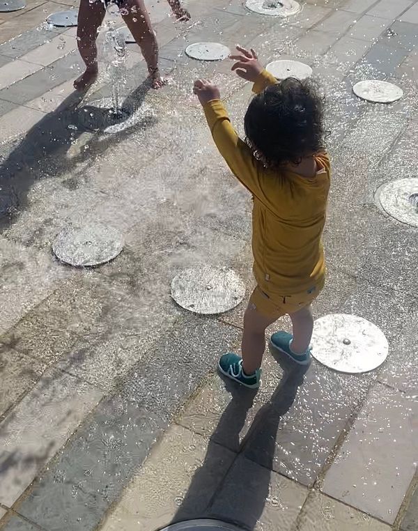 A man and his young daughter are playing and cooling off in a public fountain on a sunny day.