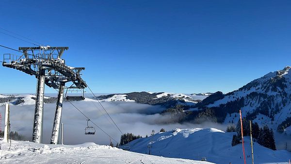A scenic view of a ski resort with a ski lift and snow-covered mountains under a clear blue sky.
