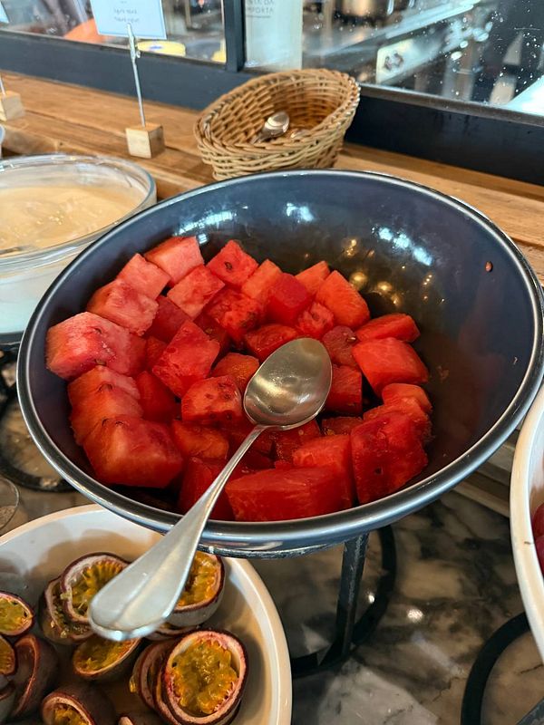 A bowl of cut watermelon is displayed alongside passion fruit in a breakfast setting.