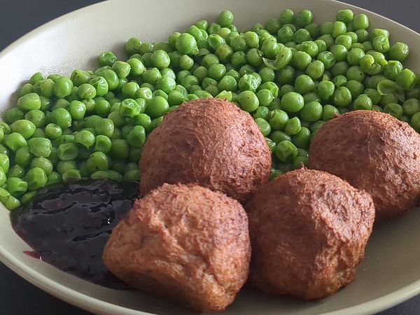 A plate features green peas and three custom meatballs with a side of sauce.
