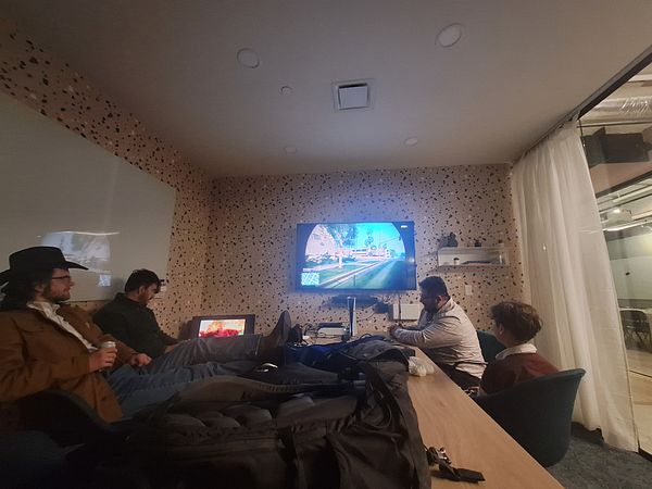 A group of friends is gathered in a coworking space, playing video games while a child participates.