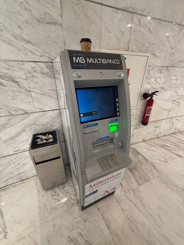A newsstand in Portugal displays various magazines including The Economist, situated at the street corner with a payment terminal visible.