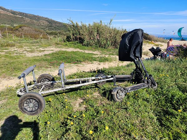 An electric scooter with a trailer is parked on a grassy area near the beach.