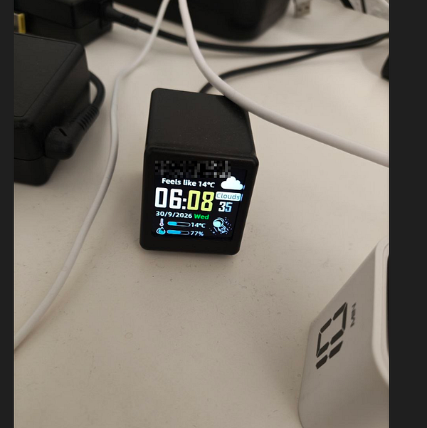 A small digital cube clock on a desk displays the time, date, weather, and humidity information.