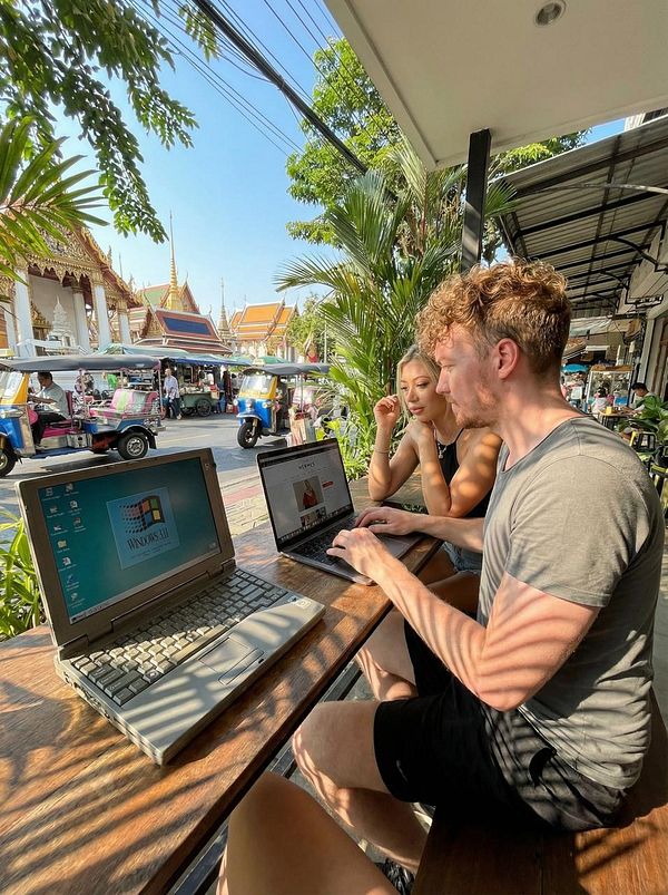 A vibrant outdoor workspace scene featuring two individuals working on laptops at a café.