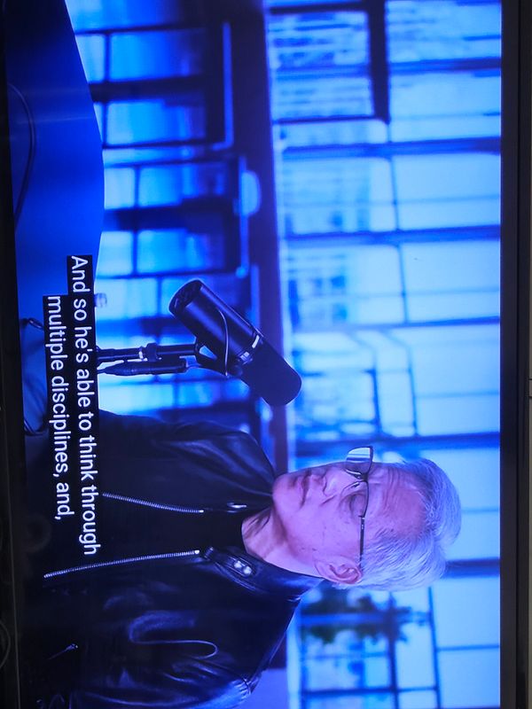 A man and a woman sit closely on armchairs in a casual setting, casually smiling and engaging with each other.