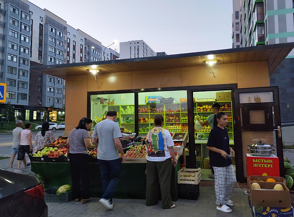 A bustling fruit market scene with several people shopping and interacting.