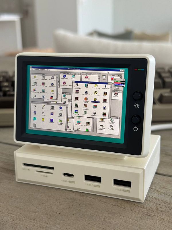 A vintage mini computer displays a retro graphical user interface on its screen.