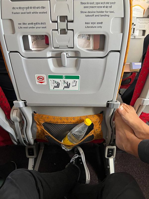 The image captures the view from a passenger's seat on an airplane, focusing on the seatback in front and the passenger's feet.