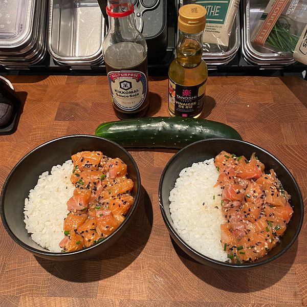 Two bowls of rice topped with salmon and condiments are displayed on a wooden surface.