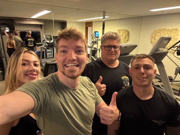 A group of four people poses for a selfie in a gym setting.