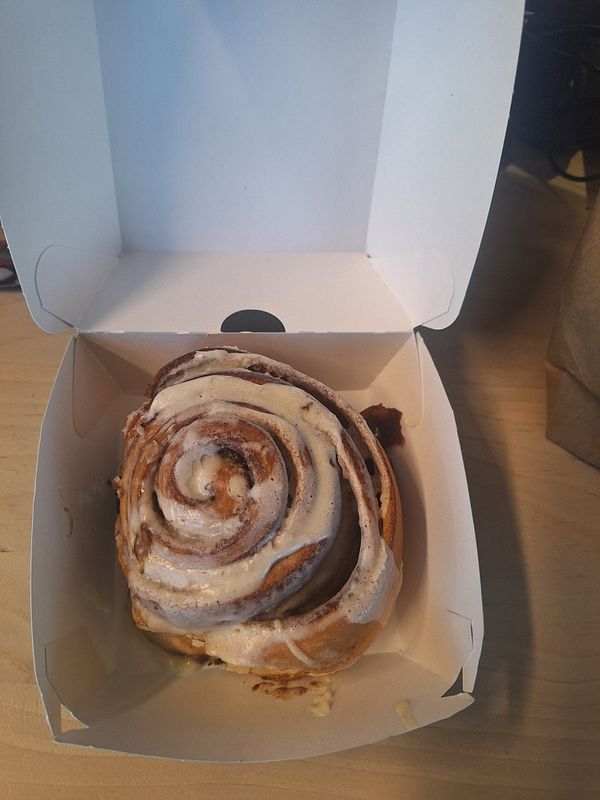 A delicious Cinnabon cinnamon roll is presented in a white takeout box.