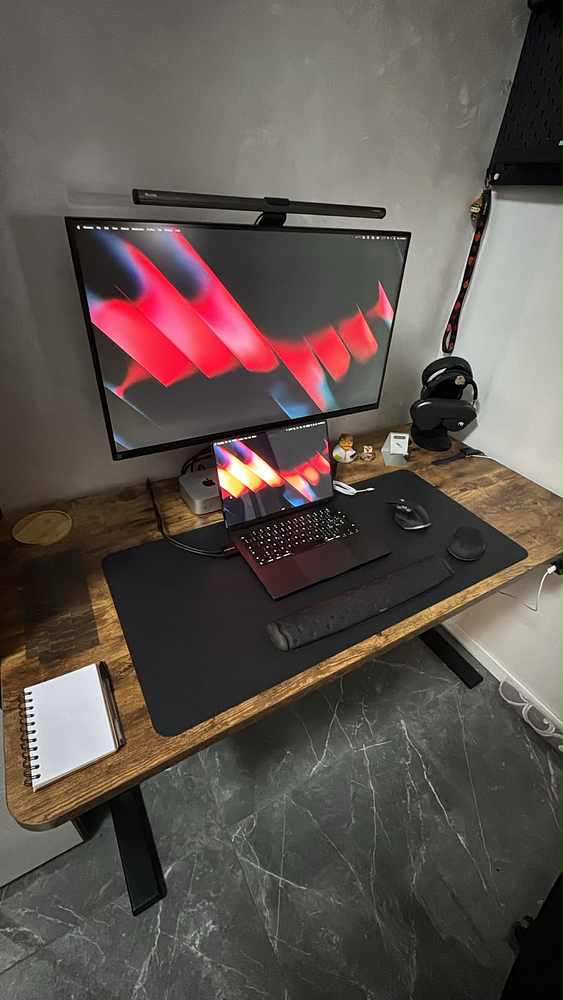 A workspace with a single widescreen computer monitor on a desk displaying a minimalistic geometric wallpaper.