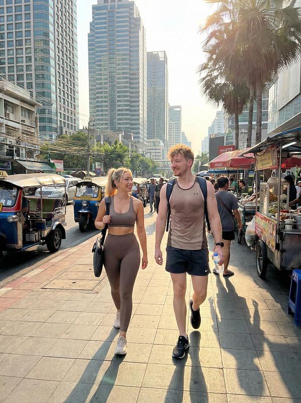 A couple walks hand-in-hand along a bustling city street lined with tall buildings and food vendors.