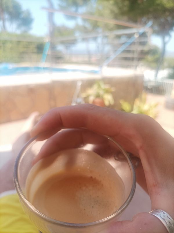 A hand holding a glass of espresso with a scenic outdoor background.
