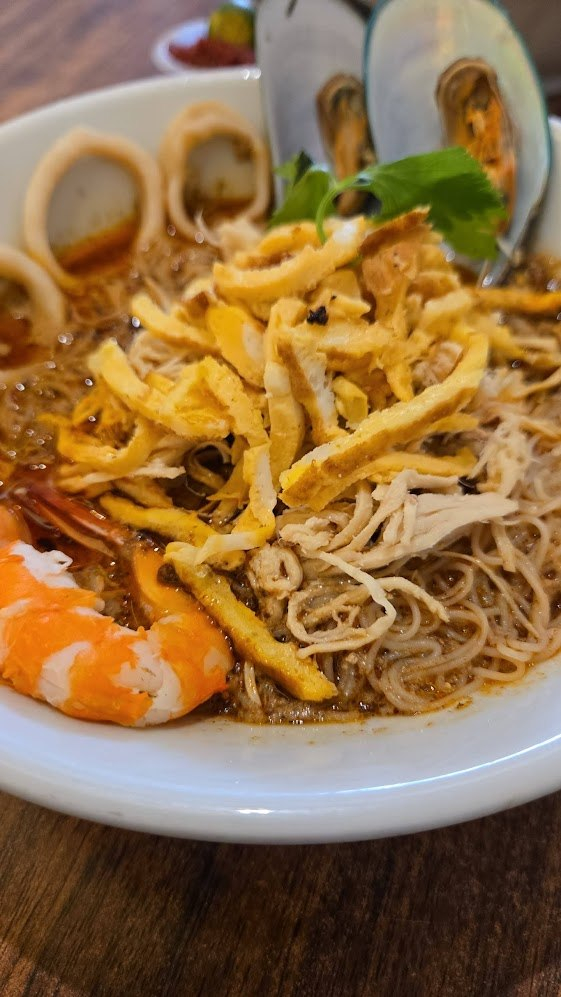A dining table filled with a variety of traditional Malaysian dishes surrounded by people enjoying a meal.