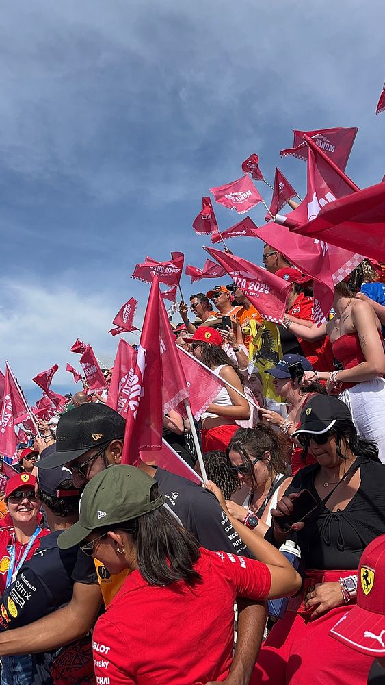 A vibrant crowd of Formula 1 fans at the Monza race, waving red flags and wearing team merchandise.