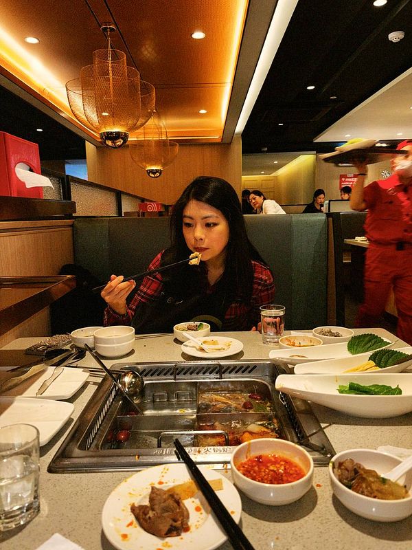 A woman enjoys a meal at a Szechuan hot pot restaurant, surrounded by various dishes and ingredients.