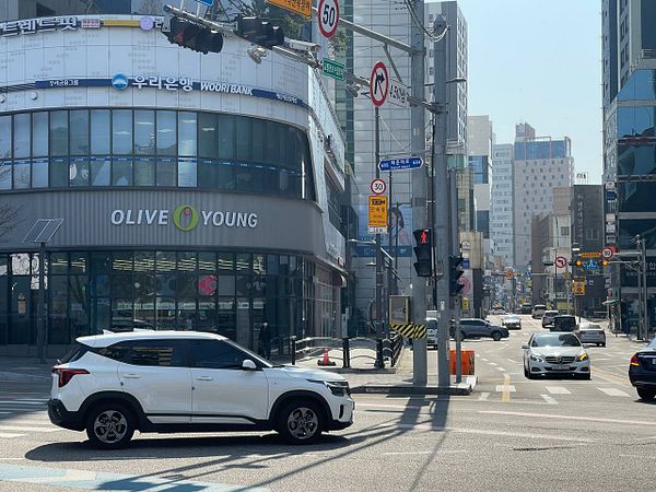 A busy urban street scene featuring a white car and various storefronts.