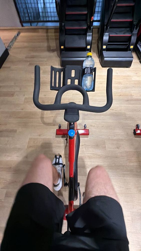 A man wearing gym attire performs an exercise with a dumbbell in a gym room with yoga mats and mirrors.