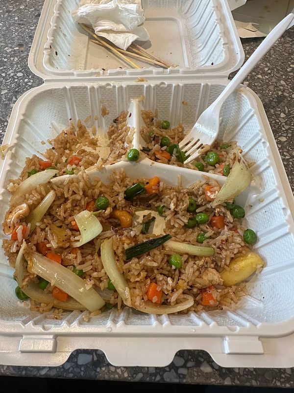 A partially eaten serving of pineapple fried rice in a takeout container.