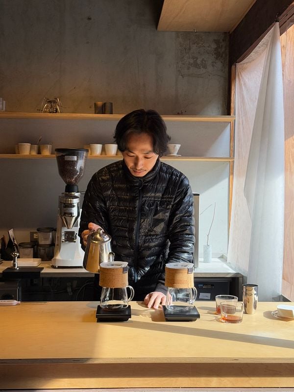 A barista prepares coffee in a minimalist café setting in Kyoto.