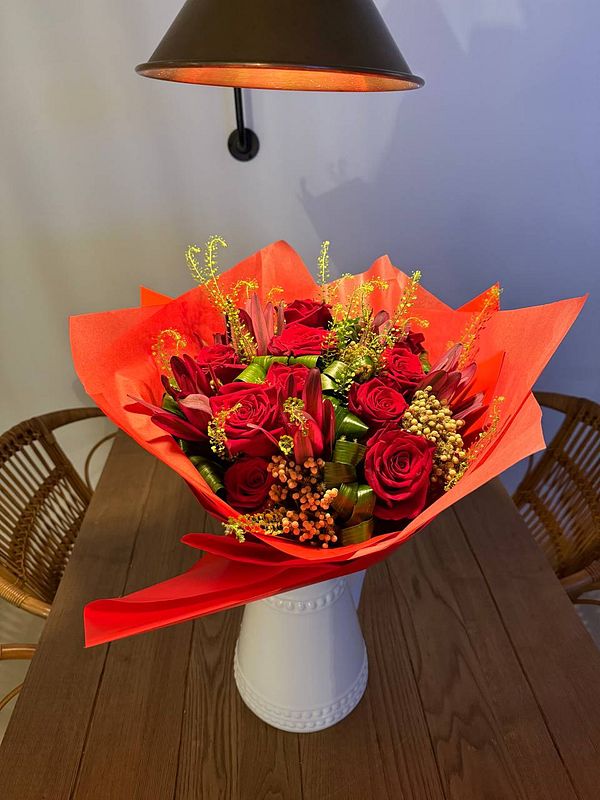 A vibrant bouquet of red roses and assorted flowers is displayed on a wooden table.
