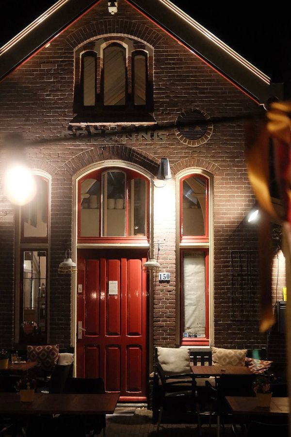 A charming restaurant exterior illuminated at night, featuring a red door and cozy outdoor seating.