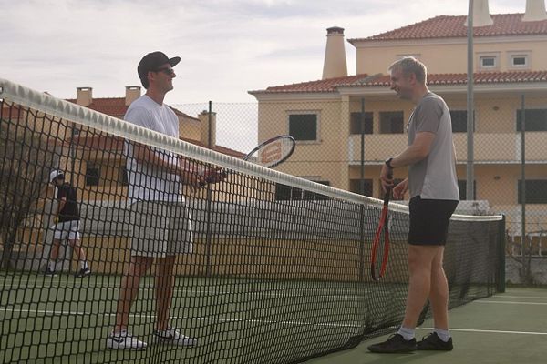 A male tennis player in mid-swing on an outdoor tennis court during daytime.