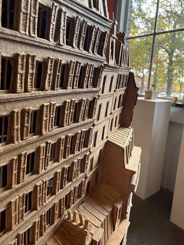 A detailed architectural model of a building made from cardboard is displayed in a well-lit interior space.