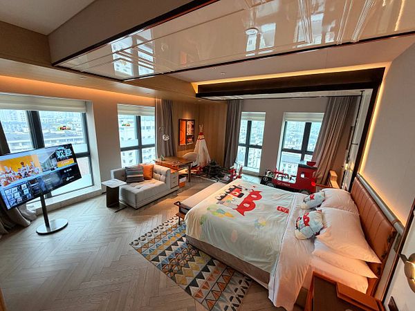 A hotel room interior with a modern, cozy design featuring a bed, wall art, and ambient lighting.