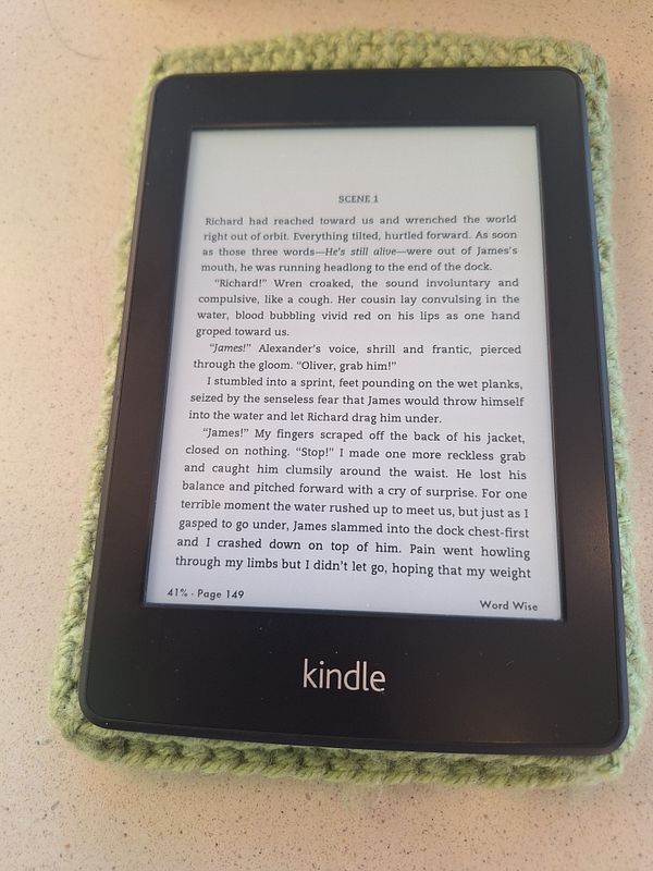 A laptop setup on a table shows a white keyboard, a smartphone with a colorful keyboard, and a green plant next to a window with curtains.