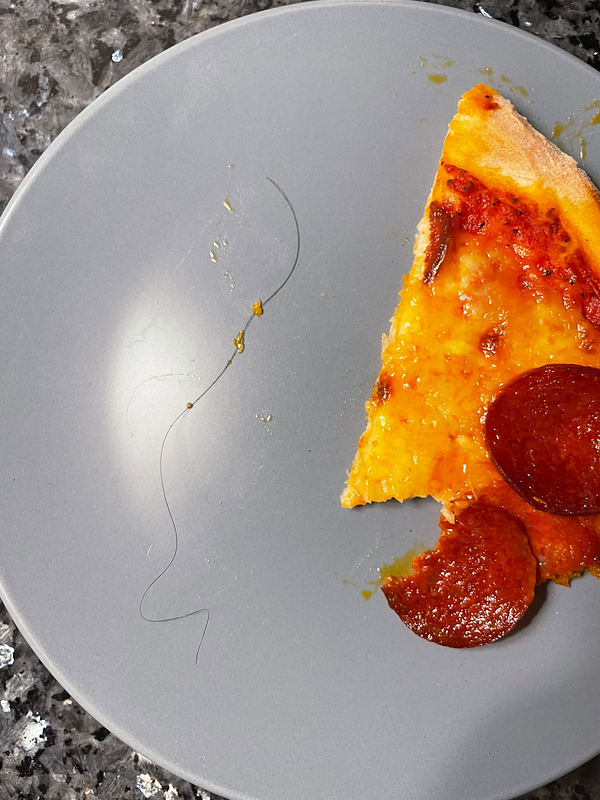 A slice of pepperoni pizza on a gray plate with a long hair next to it.