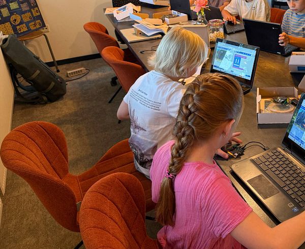 A group of children is engaged in programming activities at a table in a classroom setting.