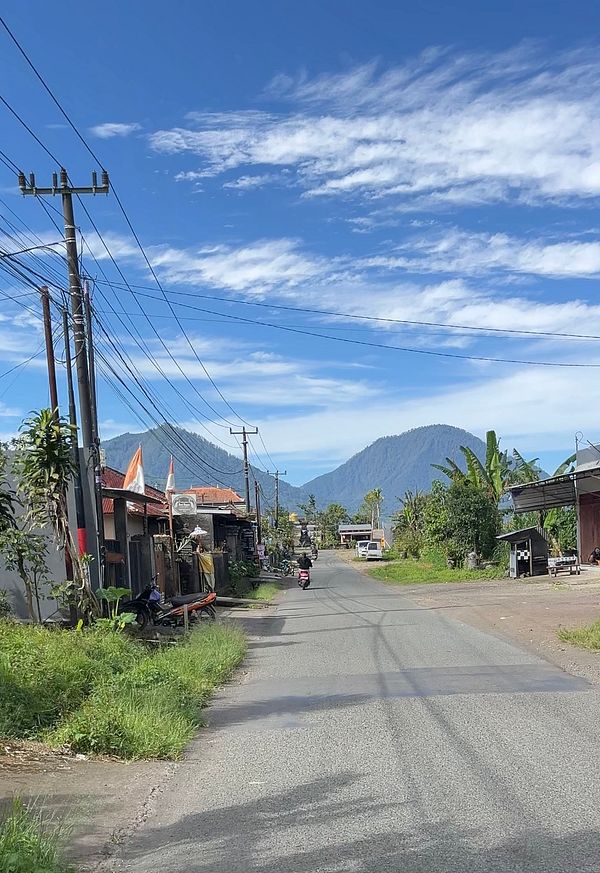 A scenic road view in Bali, showcasing local shops and mountains in the background.