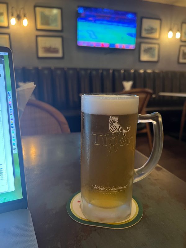 A glass of Tiger beer placed on a table, next to a black cardholder and some receipts or papers.