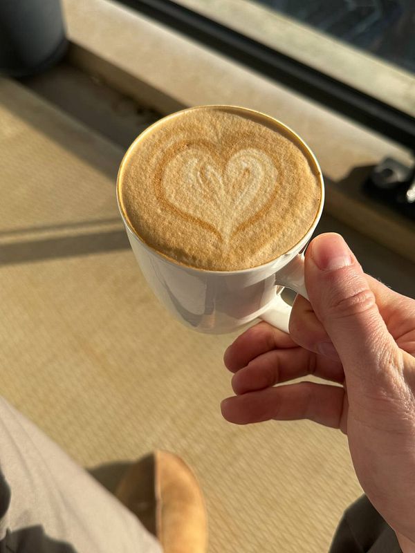 A person sitting on a sunny balcony working on a laptop with a notebook and coffee nearby.