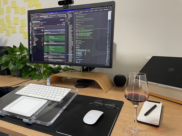 A glass of red wine sits on a wooden table illuminated by warm light in a cozy setting.