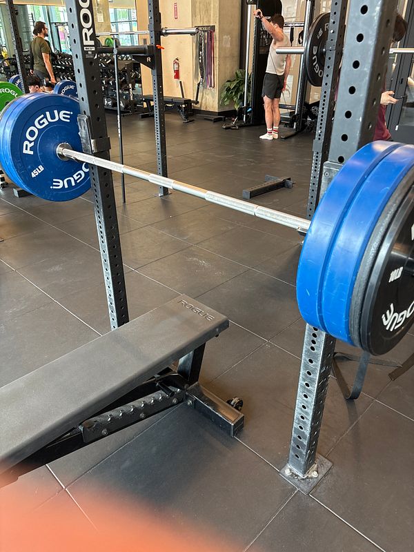 A weight bench with a loaded barbell in a gym setting.
