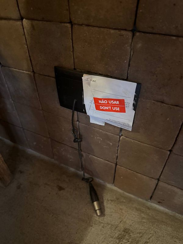 A wall-mounted power outlet is covered with a warning sign and a handwritten note.