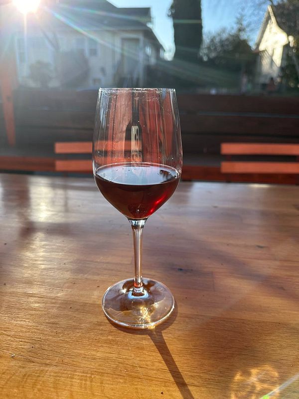 A glass of chilled Greek wine is placed on a wooden table, illuminated by sunlight.